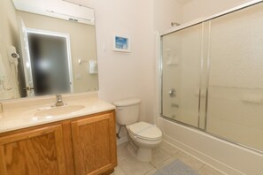 A bathroom with a wooden vanity, a toilet, a glass shower enclosure, and a mirror. - 3000yl (Kissimmee)
