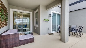 Ein moderner Patio-Bereich mit Korbmöbeln, einer Glastür, die auf einen Balkon führt, und einem kleinen Tisch mit Stühlen.