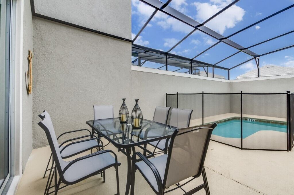 A glass-enclosed patio with a pool, outdoor seating, and a clear view of the sky.