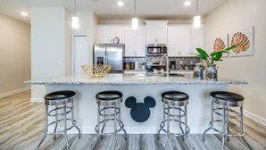 Eine moderne Küche mit weißen Schränken, Edelstahlgeräten, einer Marmorarbeitsplatte und einem Barbstuhl im Mickey-Mouse-Design.