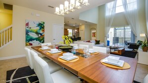 A modern dining area with a wooden table set for six, white chairs, and a contemporary chandelier. - Fantastic Resort 5 Bed 5 Bath Villa With Pool (Kissimmee)