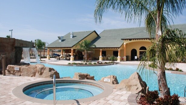 A pool area with a hot tub, palm trees, and a building with a tiled roof. - Fantastic Resort 5 Bed 5 Bath Villa With Pool (Kissimmee)