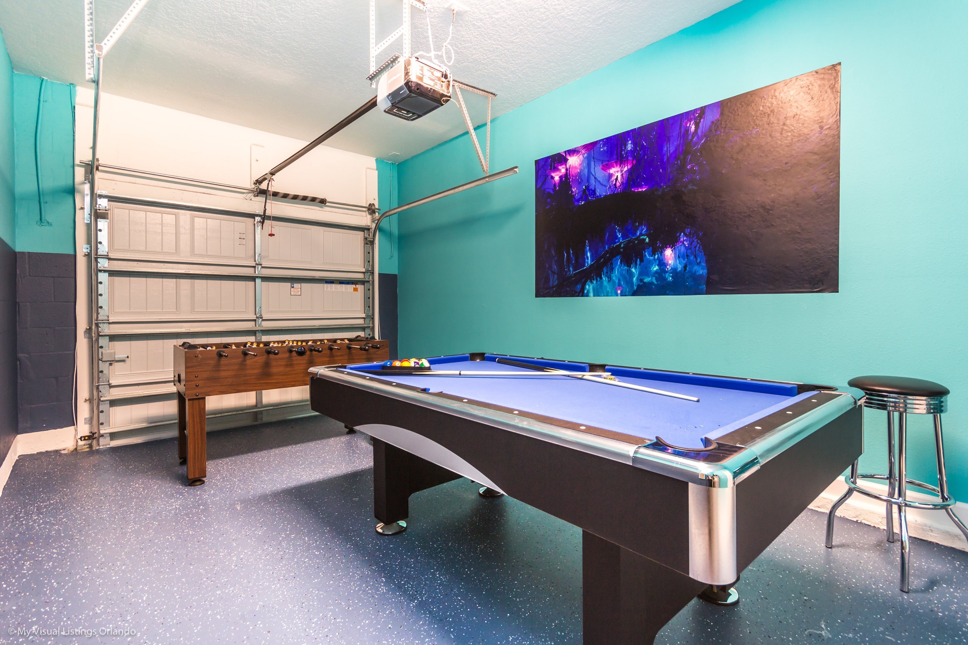 Een biljart in een kamer met teal muren, een wandprojector en een houten bank.