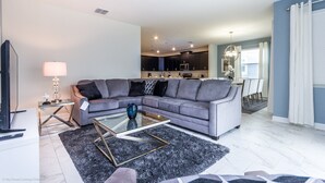 A modern living room with a grey sectional sofa, a glass coffee table, and a TV on a stand.
