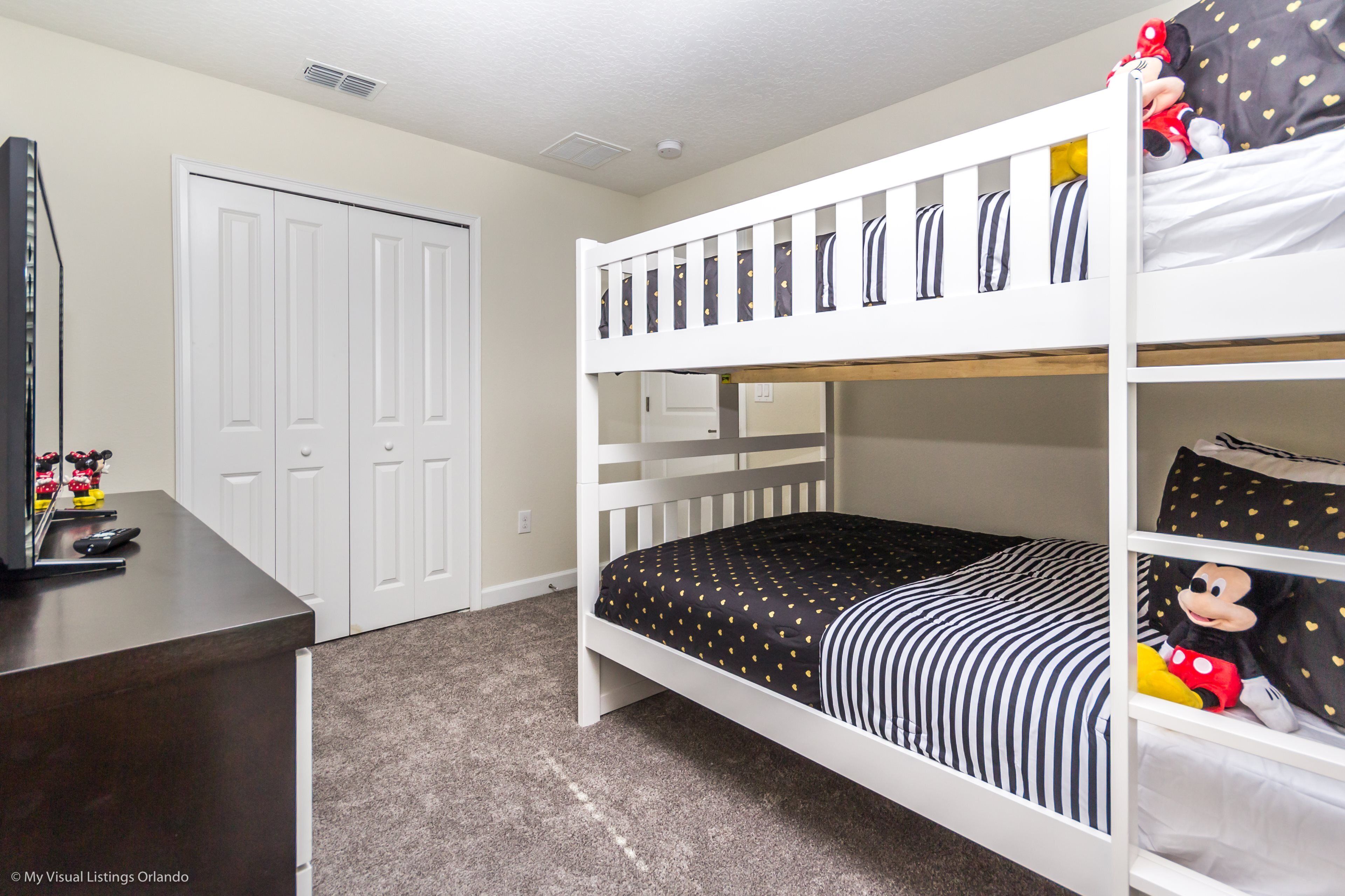 A bunk bed with a black and white striped bedspread, a white wardrobe, and a desk with a computer and toys.