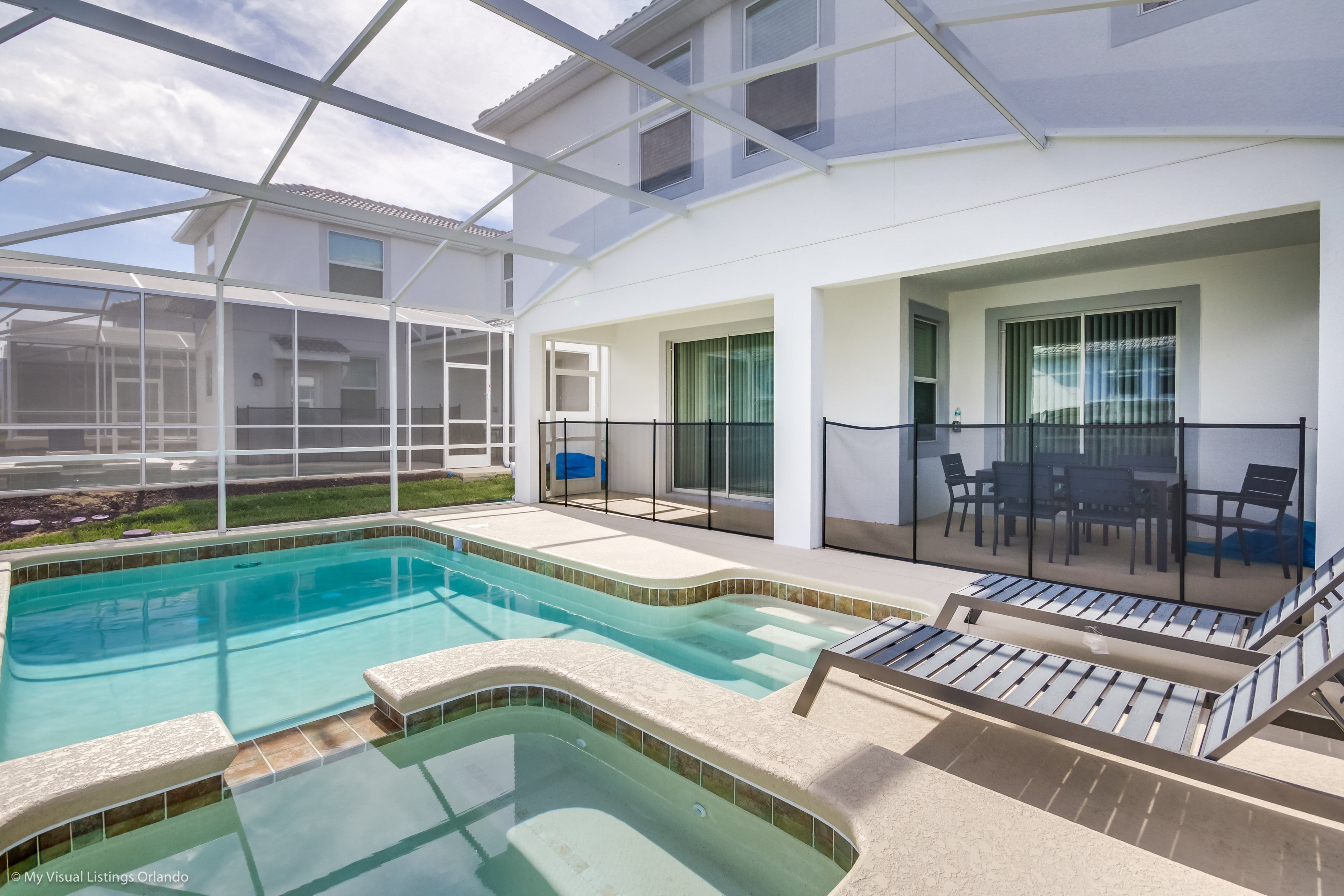 A swimming pool with a glass enclosure, lounge chairs, and a patio area with outdoor furniture.