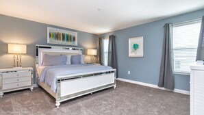 A bedroom with a bed, nightstands, a dresser, a ceiling light, and a window with curtains.