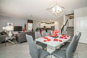 Una sala de estar moderna con comedor, muebles grises, un televisor y una escalera que sube a un nivel superior.