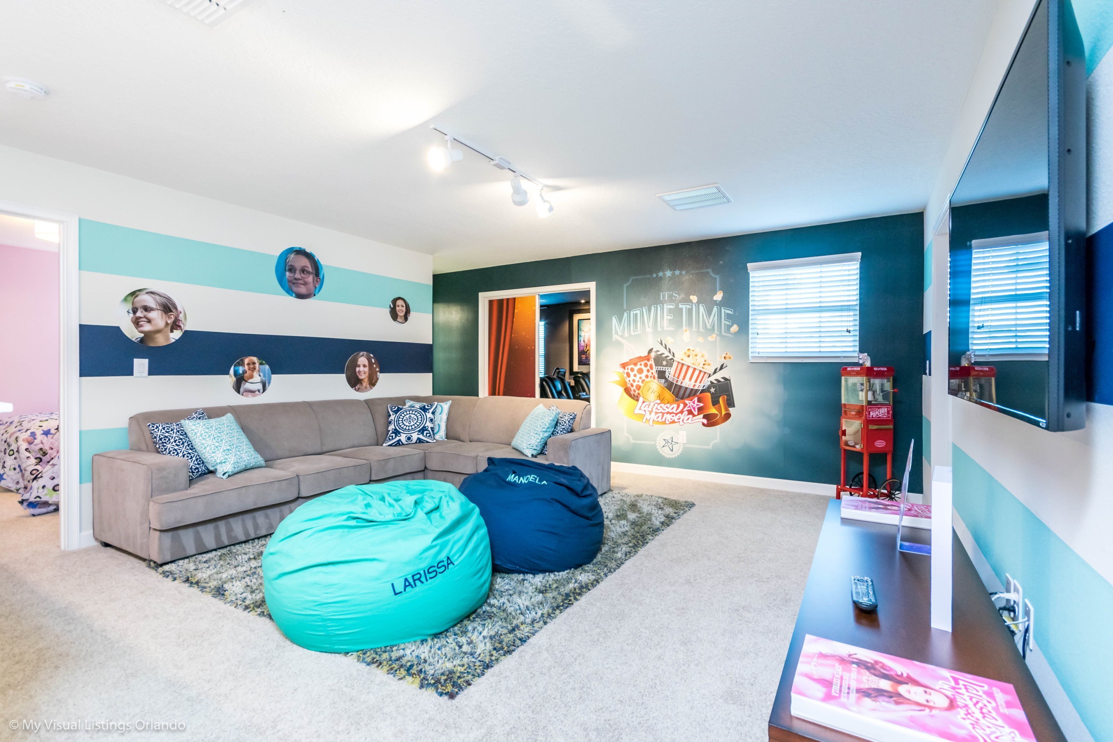 Ein modernes Wohnzimmer mit Ecksofa, Sitzsäcken, einem Flachbildfernseher und einer Wand mit Filmdekorationen.
