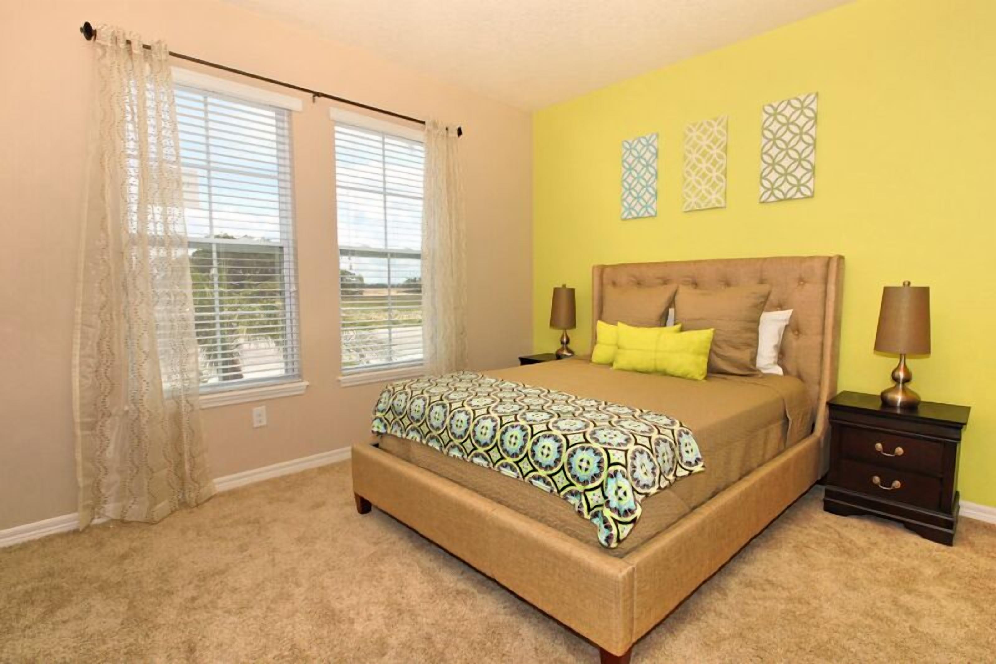 A bedroom with a bed, curtains, a nightstand, and wall art.