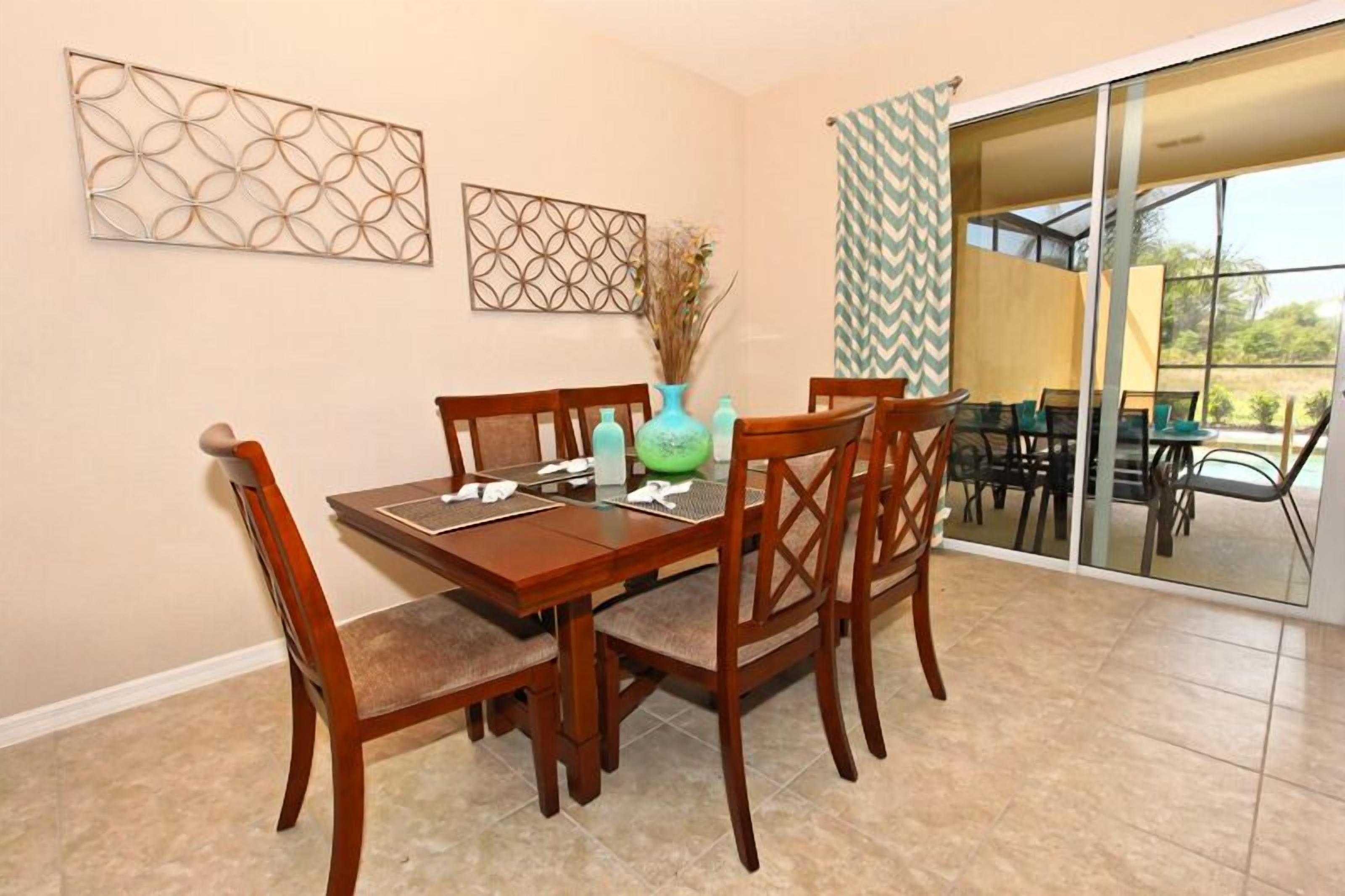 A dining area with a wooden table and chairs, a vase with dried flowers, and two wall art pieces.