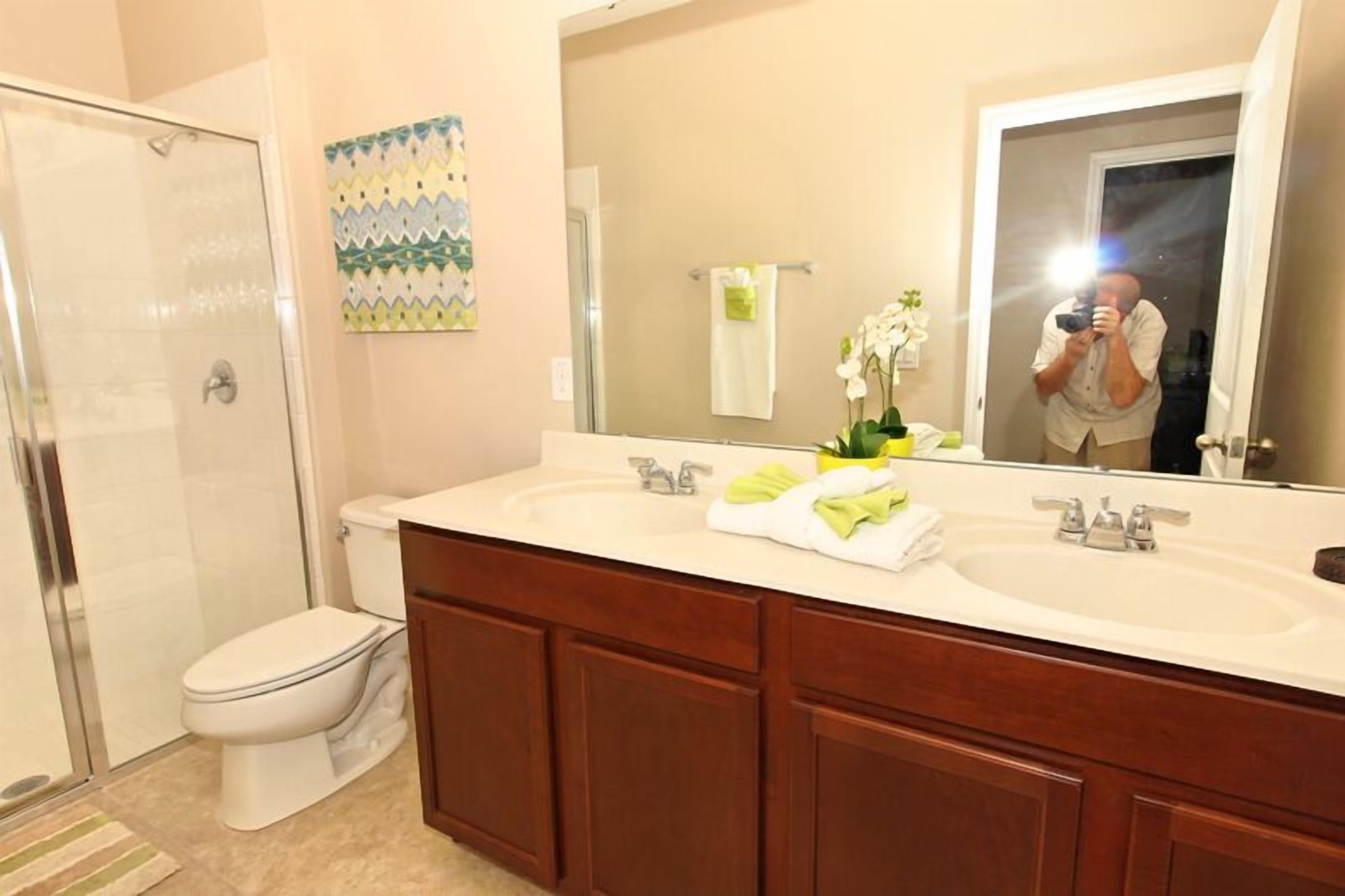 A bathroom with a shower, toilet, and double sink vanity.