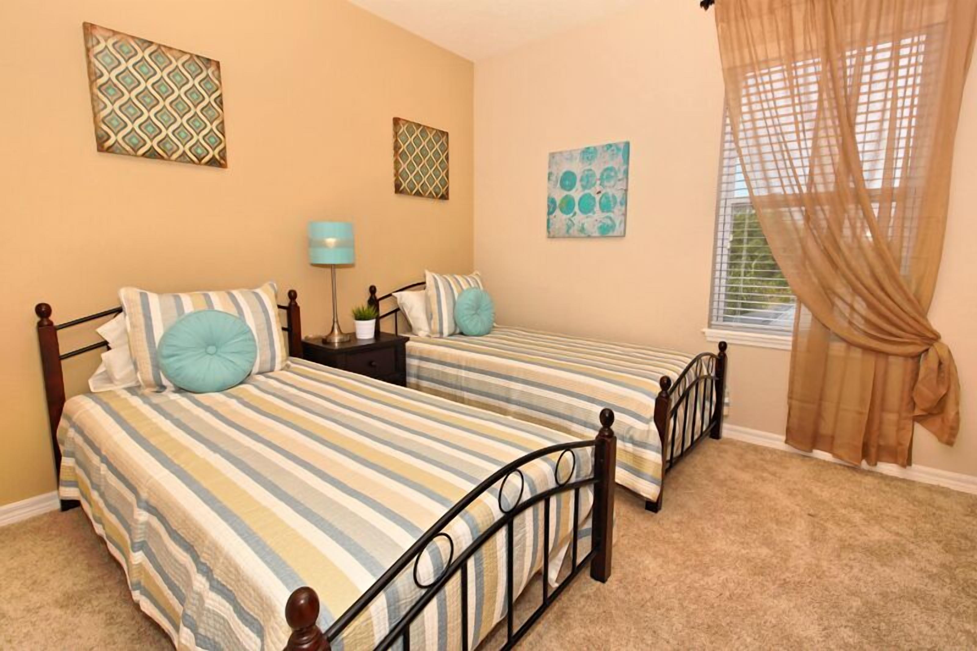 A bedroom with two beds, a nightstand, a lamp, and a window with curtains.