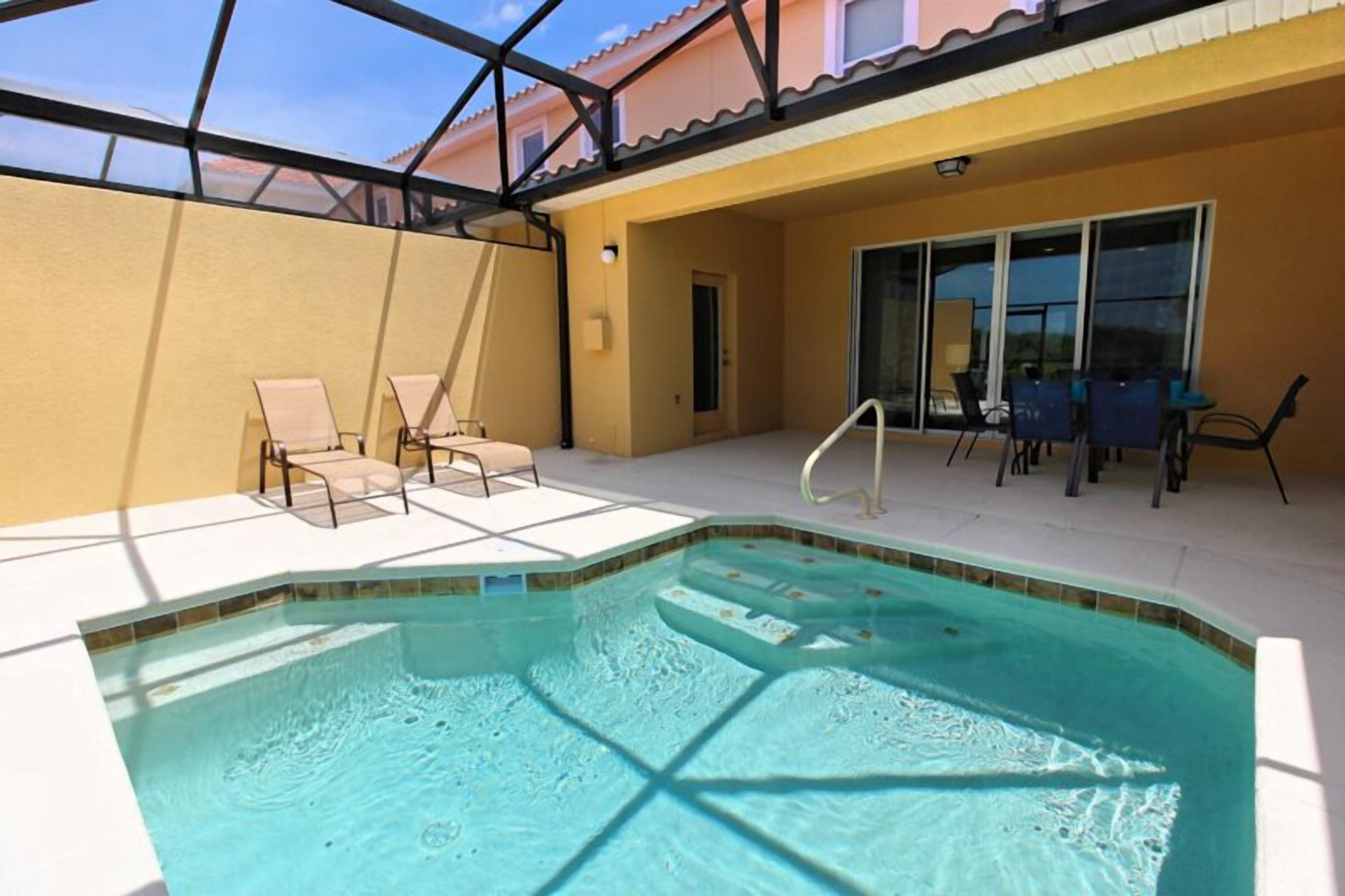 Una piscina interior con sillas de descanso y una mesa, rodeada por un cerramiento de vidrio.