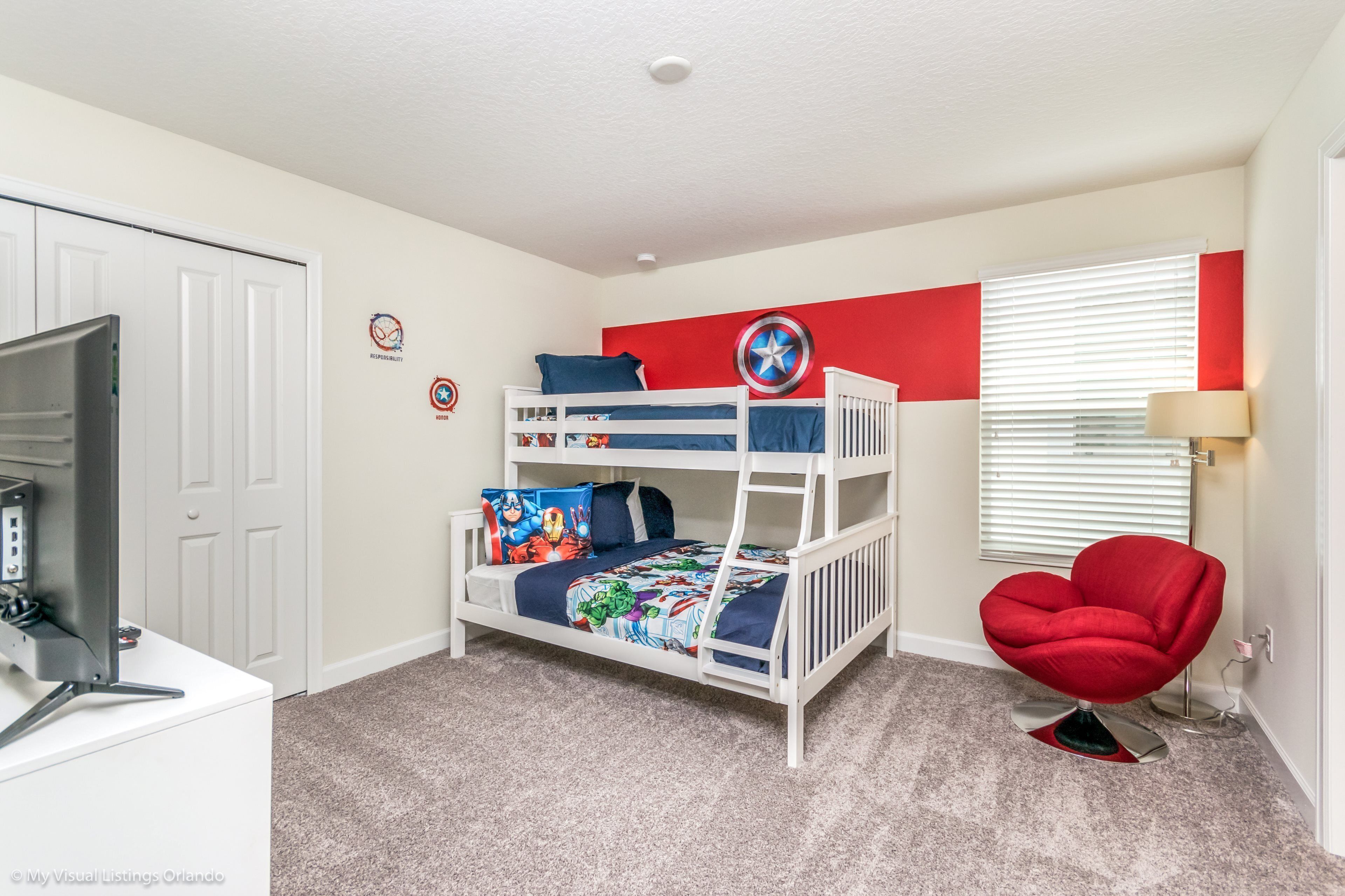 A room with bunk beds, a red chair, a television, and a window with blinds.