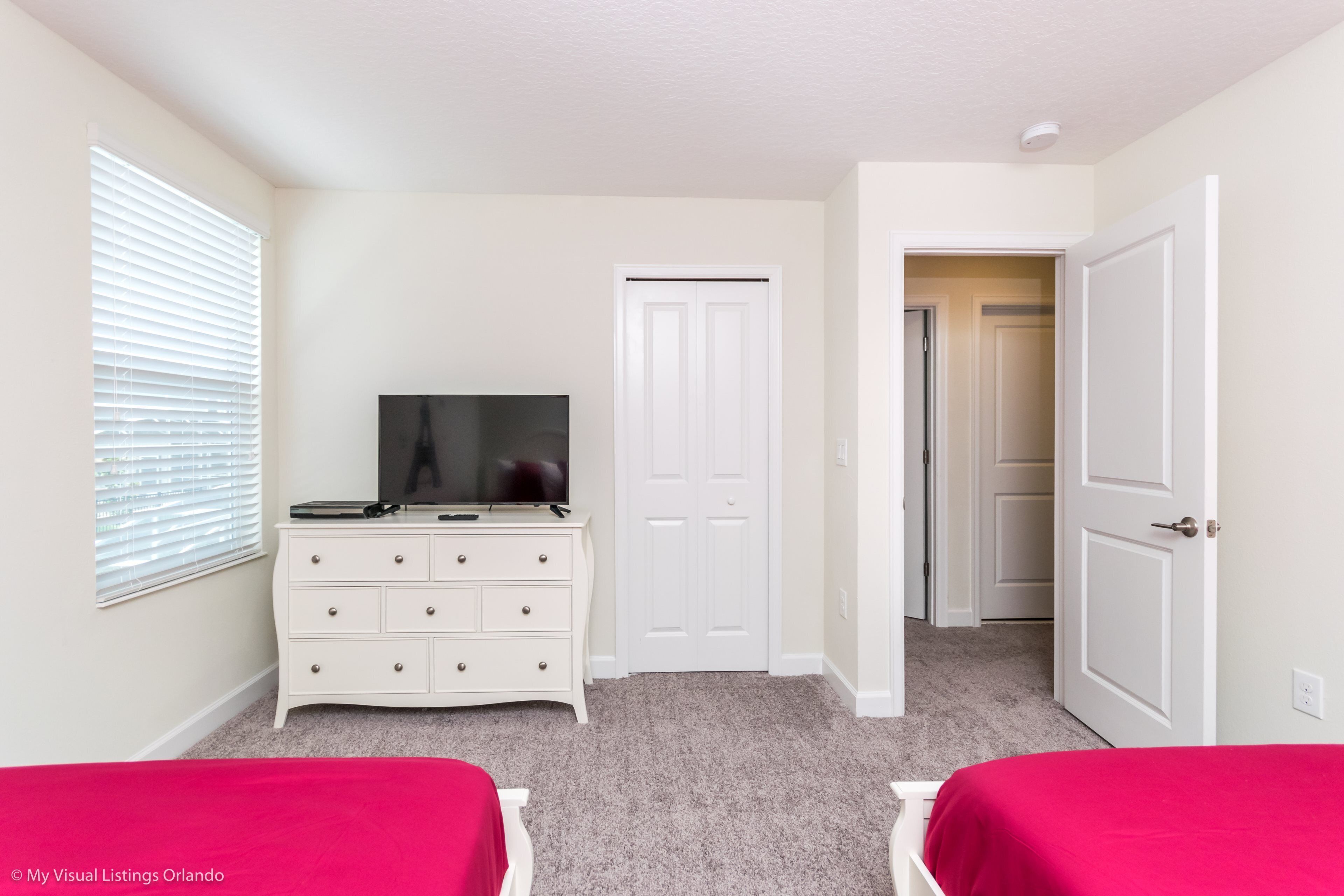 A bedroom with a white dresser, a television, and two beds with red bedding.