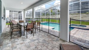 A covered patio with a pool, glass walls, and a brick floor.