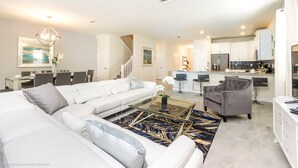 A spacious living room with a white sofa, a coffee table, and a gray armchair. A staircase leads to an upper level.