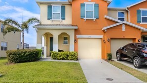 A two-story residential building with a beige and orange facade, a garage, and a black car parked in the driveway. - 3175tc Amazing Compass Baytown Home Sleeps 10 (Kissimmee)