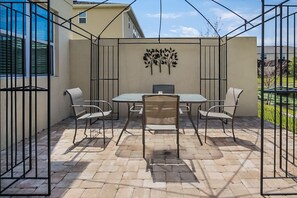 A patio area with a table and chairs, a decorative wall, and a view of a residential building. - 3175tc Amazing Compass Baytown Home Sleeps 10 (Kissimmee)