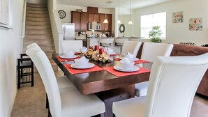 A dining area with a wooden table set for six, surrounded by white chairs. - 3175tc Amazing Compass Baytown Home Sleeps 10 (Kissimmee)