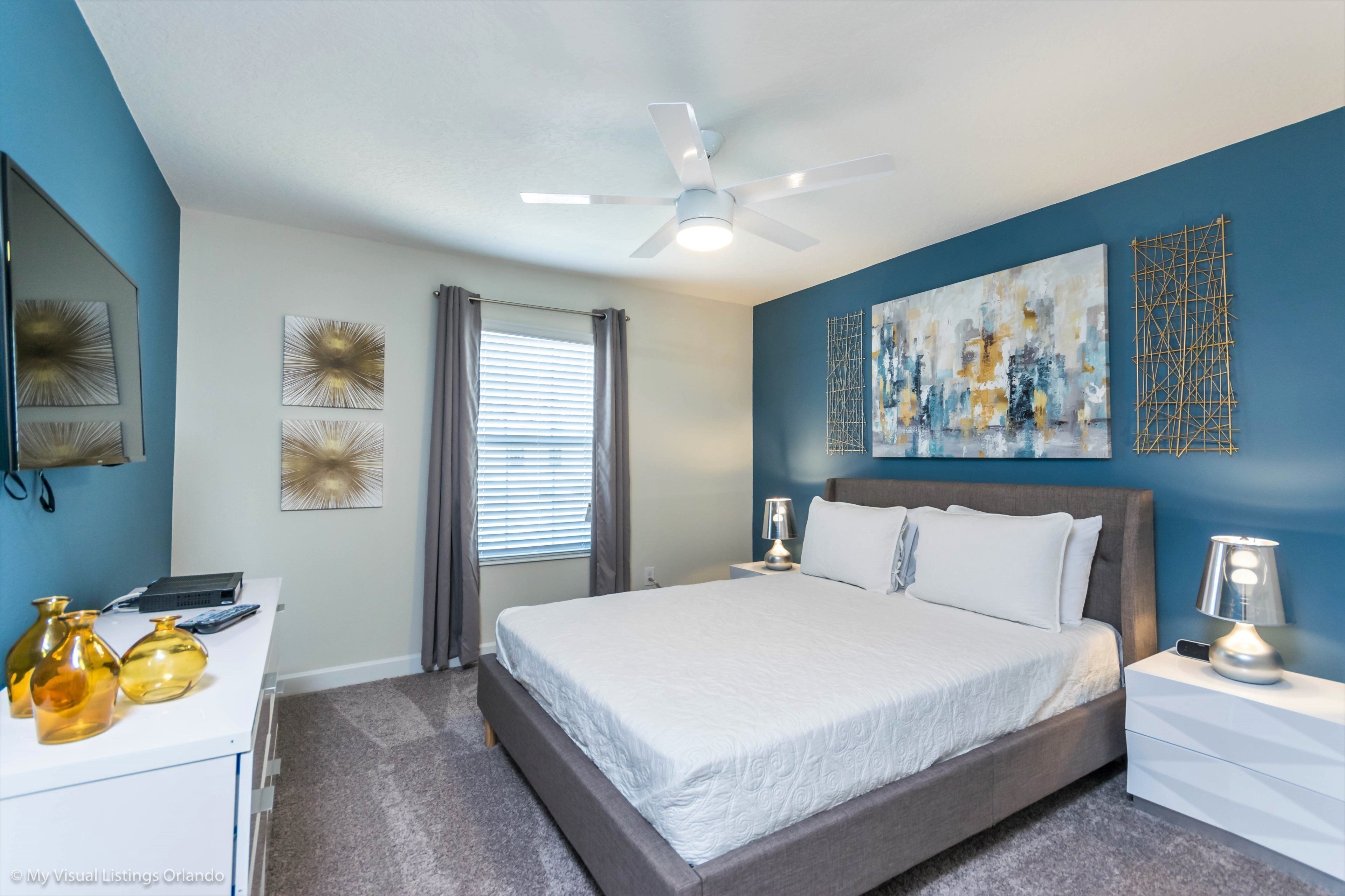 A bedroom with a bed, bedside tables, a desk, and a ceiling fan.
