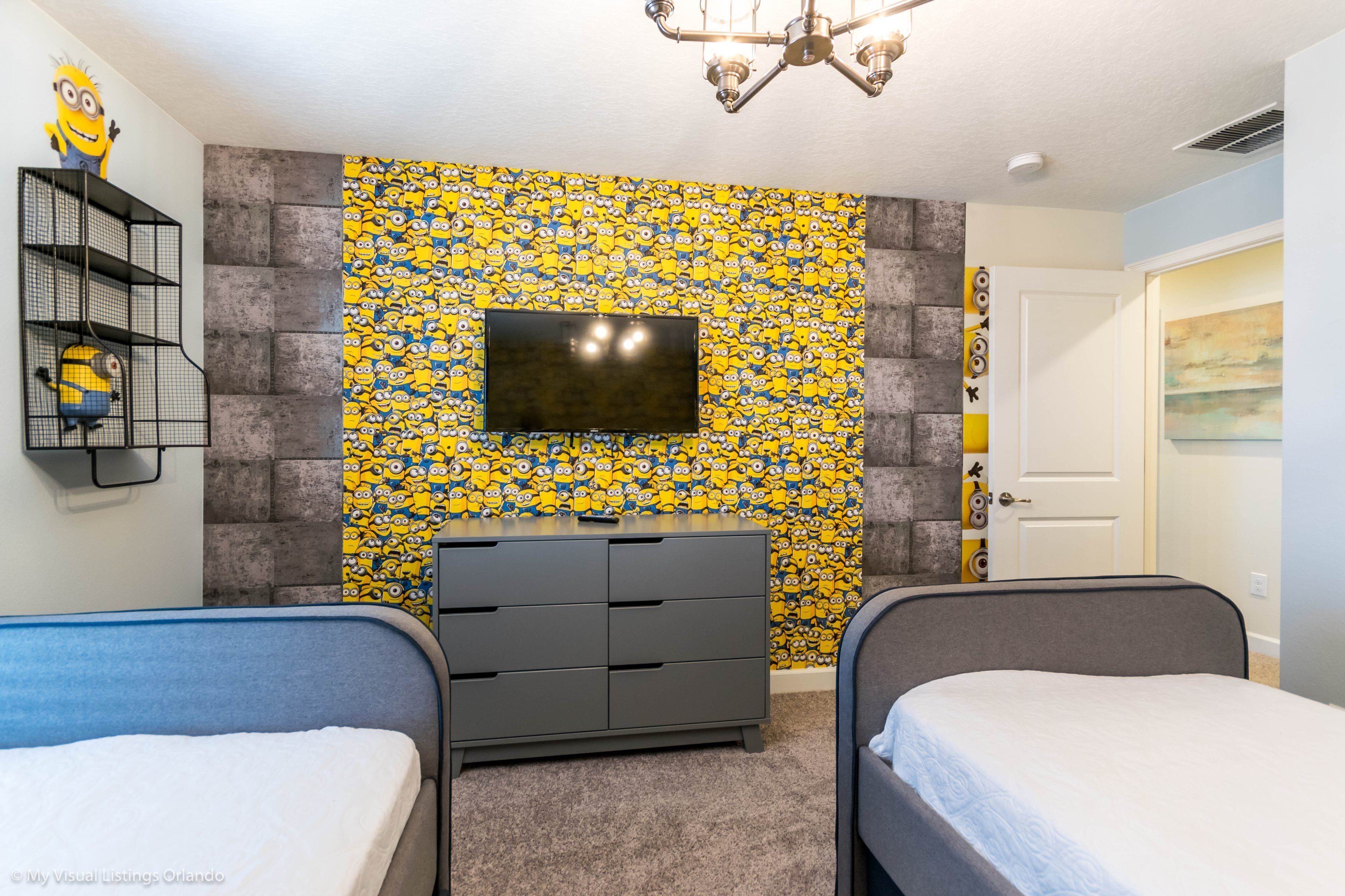 A bedroom with two beds, a TV, and a Minion-themed wallpaper.