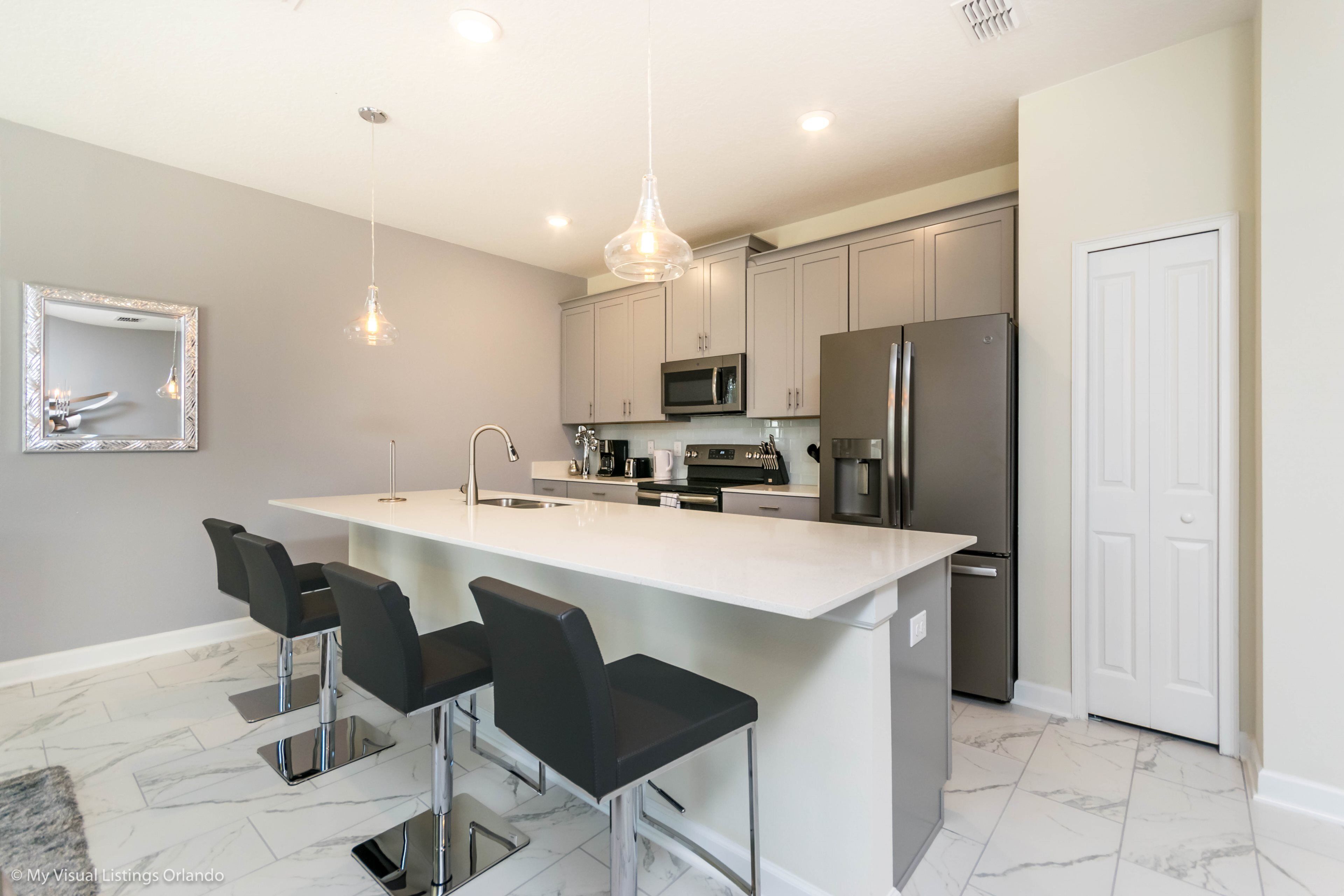 A modern kitchen with a central island, bar stools, stainless steel appliances, and pendant lighting.