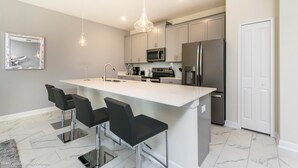 Une cuisine moderne dotée d’un îlot central, de tabourets de bar, d’appareils électroménagers en acier inoxydable et de luminaires suspendus.