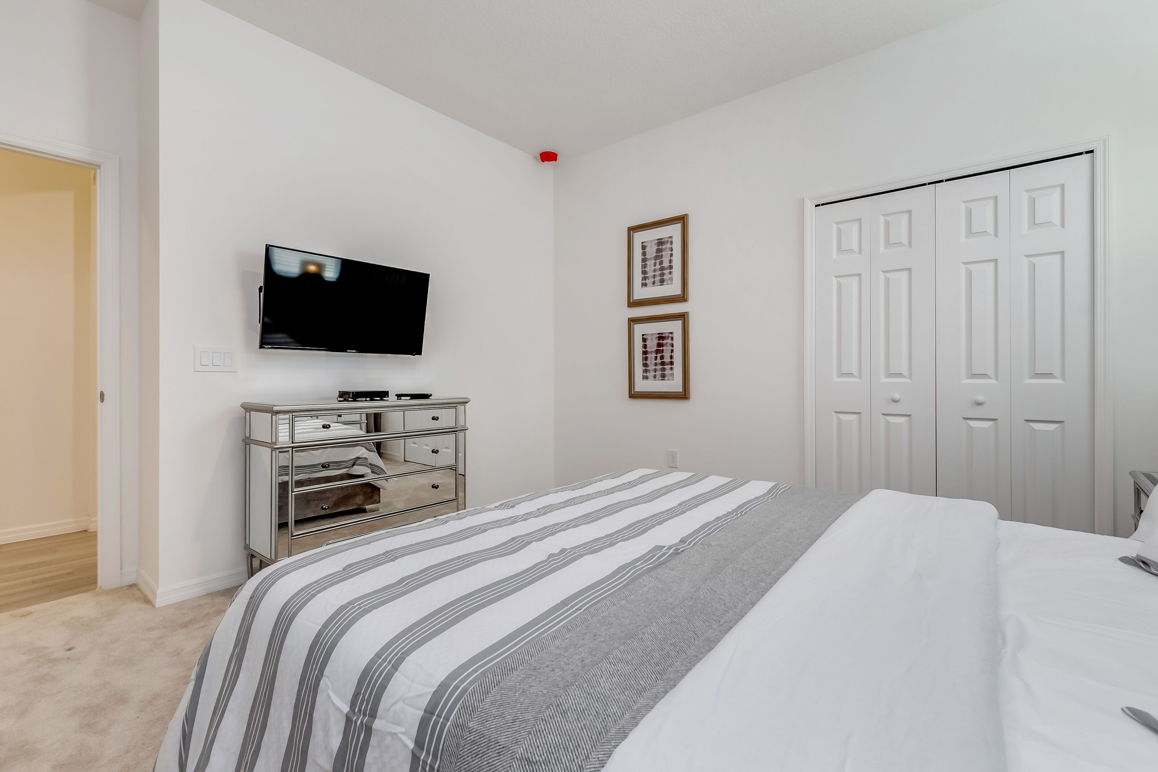 A bedroom with a bed, a TV mounted on the wall, a dresser, and a closet.