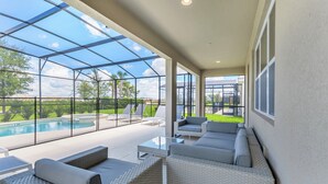 A modern outdoor lounge area with a glass enclosure, comfortable seating, and a view of a swimming pool. - 14 Bdrm 11 Bath Villa For 30 (Davenport)