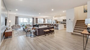 A spacious living area with a sofa, coffee table, and a dining table. There is a kitchen area with a staircase leading to an upper level. - 14 Bdrm 11 Bath Villa For 30 (Davenport)