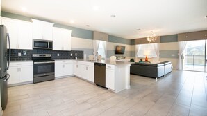A modern kitchen with white cabinets, a built-in microwave, and a dishwasher. - 1686 Champions Gate 8 Bedroom Resort Villa (Davenport)