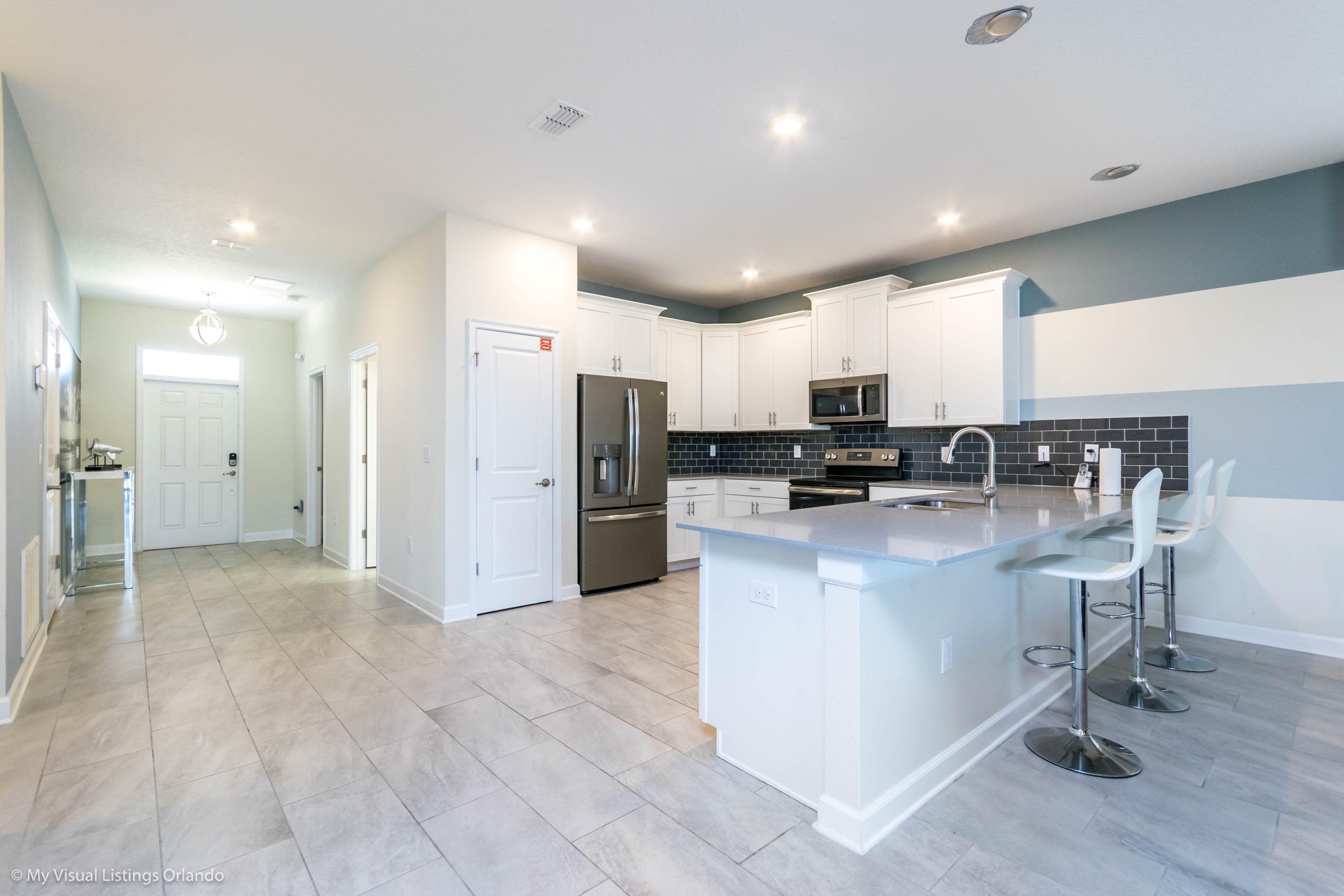 A modern kitchen with white cabinets, a stainless steel refrigerator, a microwave, and a large island with bar stools.