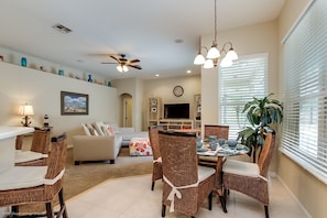 A spacious living room with a dining area, a ceiling fan, and a large window with blinds.