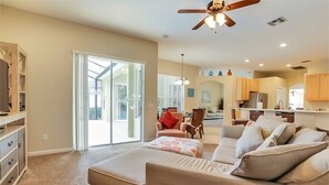 A spacious living room with a large sofa, a dining area with chairs, a kitchen with cabinets, and a ceiling fan. - Fantastically Decorated 4 bed 3 Bath (Davenport)
