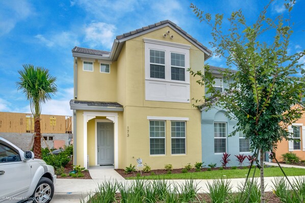 A two-story residential building with a yellow facade, white trim, and a front entrance with a door and window.