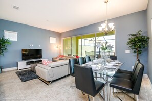 A modern living room with a dining area, featuring a sofa, a TV, and a dining table set for six.