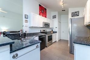 A modern kitchen with white cabinets, a granite countertop, stainless steel appliances, and a red floral artwork on the wall.