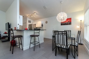 A modern kitchen with white cabinets, a central island with stools, a dining area with striped chairs, and a cityscape painting on the wall.
