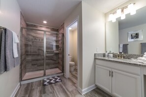 Une salle de bain moderne dotée d’une douche à parois de verre, d’un meuble-lavabo avec un plan de travail en granit et d’un grand miroir.