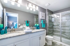 Une salle de bain moderne avec un comptoir en granit, des armoires blanches, une douche en verre et un grand miroir.