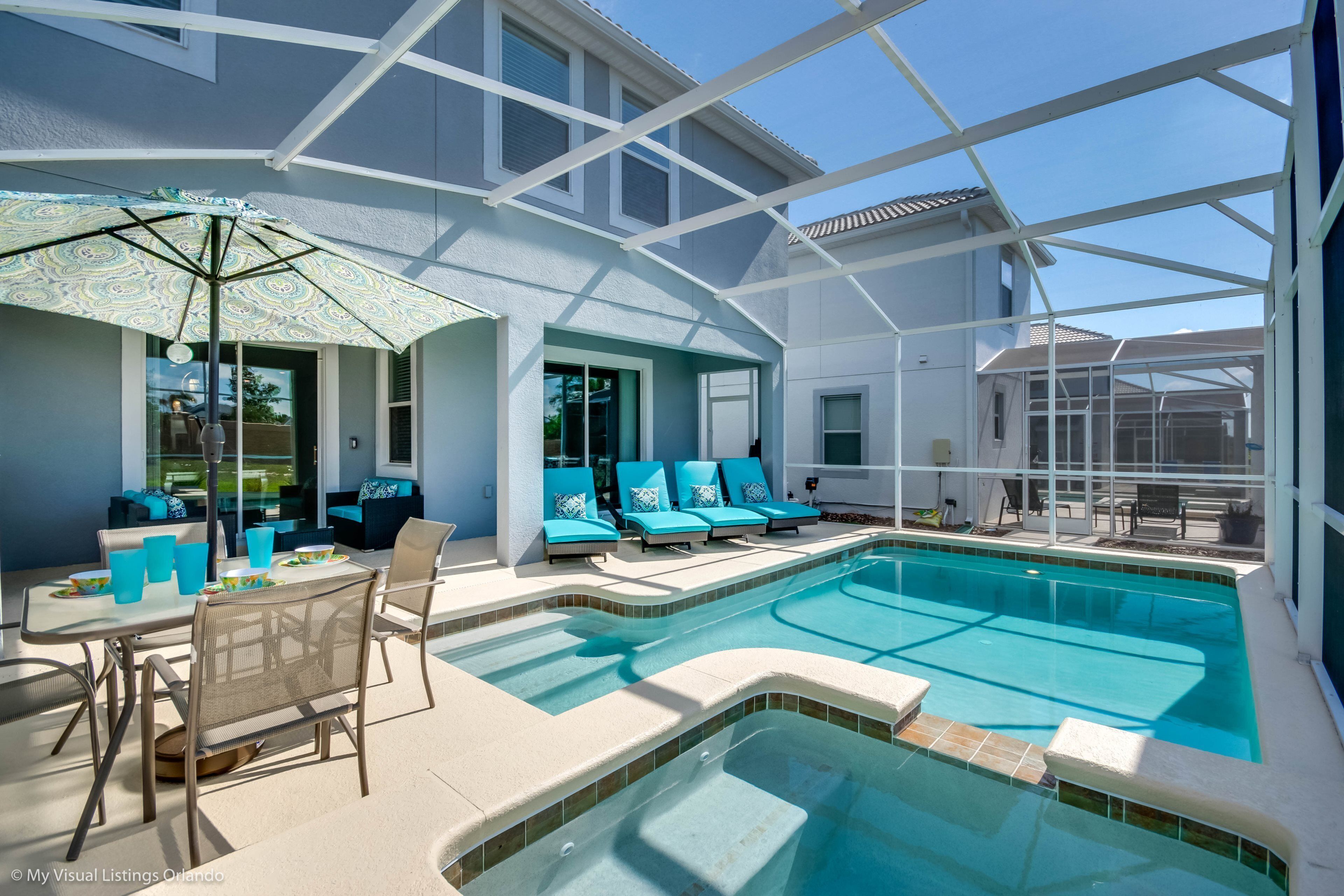 An outdoor swimming pool with lounge chairs and a table, surrounded by a covered patio area.