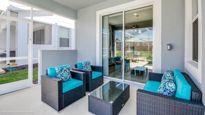 Un patio techado con mobiliario de mimbre y puertas de cristal que dan a un espacio al aire libre.