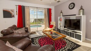 A living room with a brown leather sofa, a glass coffee table, a flat-screen TV on a white stand, a ceiling fan, and a view of a swimming pool through glass doors. - 353 Glen (Davenport)