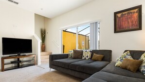 A living room with a large gray sectional sofa, a flat-screen TV on a wooden stand, a potted plant, and a painting on the wall. - Bella Vida 4570 IHR 1020 (Kissimmee)