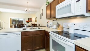 A modern kitchen with white appliances, wooden cabinets, and a central island with a sink and various kitchen items. - Bella Vida 4570 IHR 1020 (Kissimmee)