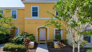 A yellow building with a central entrance, surrounded by greenery and a small garden. - Bella Vida 4570 IHR 1020 (Kissimmee)