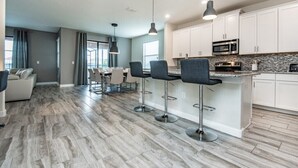 A modern kitchen with white cabinets, a granite countertop, and a built-in oven. There are three bar stools and pendant lights above the counter. - 6 Bed Villa Games Pool Spa (Davenport)
