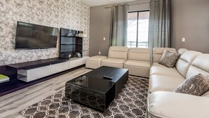 A modern living room with a flat-screen TV, a sofa, a coffee table, and a patterned rug. - 6 Bed Villa Games Pool Spa (Davenport)